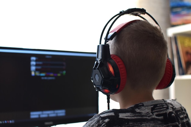 Um menino com fones de ouvido está sentado em um computador jogando jogos online. o vício do jogo infantil.