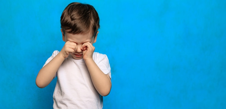 Foto um menino com fundo azul esfrega os olhos. saúde ocular. doenças oculares. um bebê chorando. fadiga de crianças. psicologia.