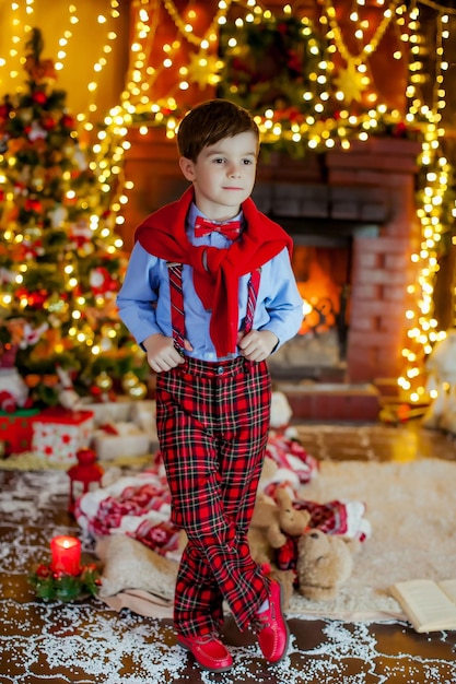 Um menino com roupas de ano novo perto da lareira na véspera de ano novo.