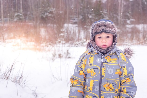 Um menino com roupas quentes está no meio de uma floresta de inverno