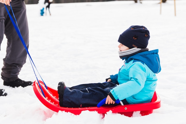 Foto um menino com trenó vermelho na neve