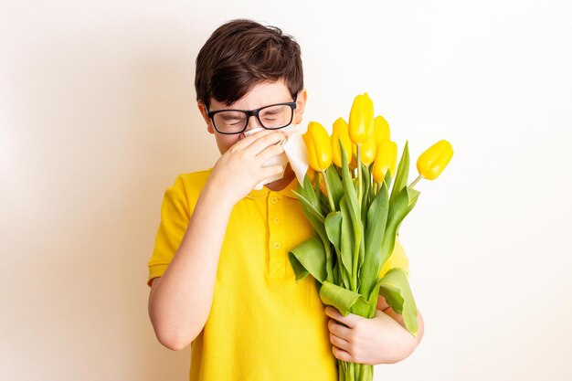 Foto um menino com um buquê de tulipas cobriu o nariz com um guardanapo de papel e espirra