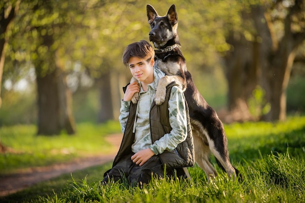 Um menino com um cachorro anda no parque em uma noite ensolarada de primavera sente-se na grama Amizade do homem e do estilo de vida saudável dos animais