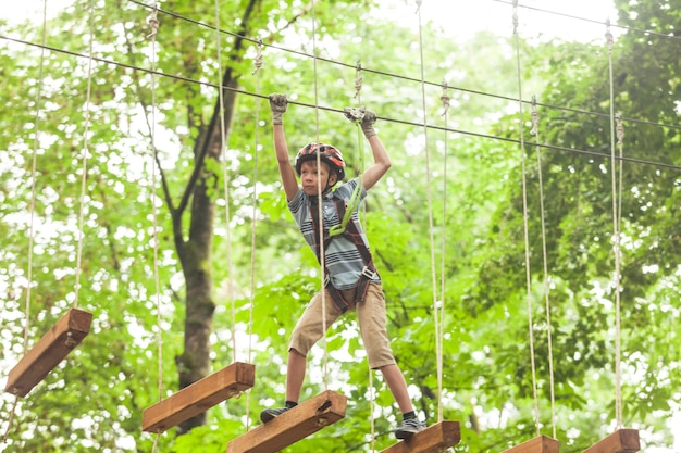 Um menino com um capacete e equipamento de segurança em um parque de cordas de aventura no fundo da natureza