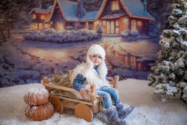 Um menino com um chapéu branco e botas no fundo de uma floresta artificial na vila de inverno