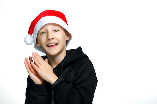 Um menino com um chapéu de Papai Noel vermelho bate palmas e ri alegremente