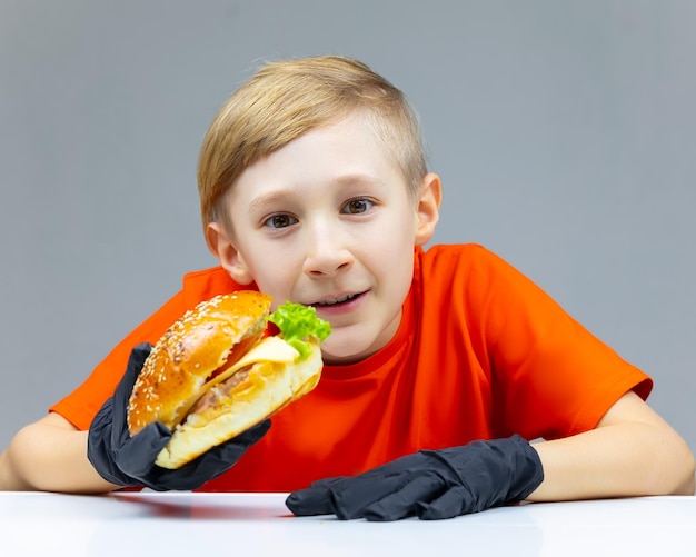 Um menino com um cheeseburger segura na mão e parece direto