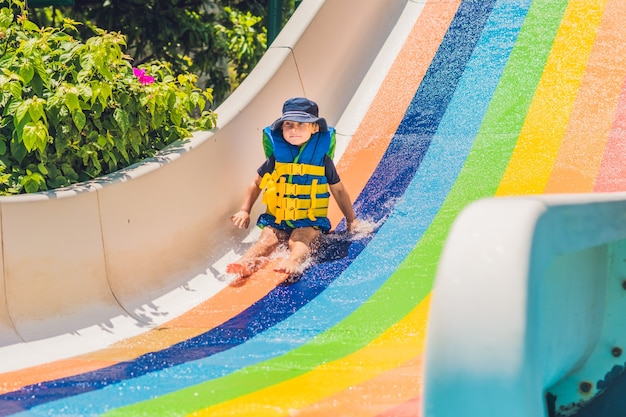 Um menino com um colete salva-vidas escorrega de um escorregador em um parque aquático.