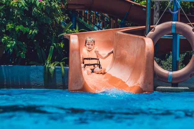 Foto um menino com um colete salva-vidas escorrega de um escorregador em um parque aquático.