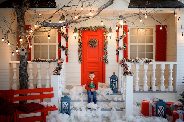 Um menino com um moletom de Natal sentado na escada de uma casa