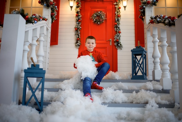 Um menino com um moletom de Natal sentado na escada de uma casa