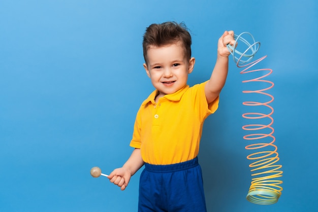 Um menino com um pirulito fica em um fundo azul de uma parede com um brinquedo. Prevenção da cárie infantil. Copie o espaço