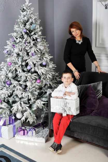 Um menino com um presente para sua mãe ao redor da árvore de Natal
