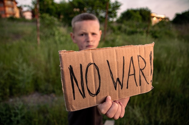 Foto um menino com um rosto sujo e olhos tristes segura um cartaz de papelão com a inscrição no war