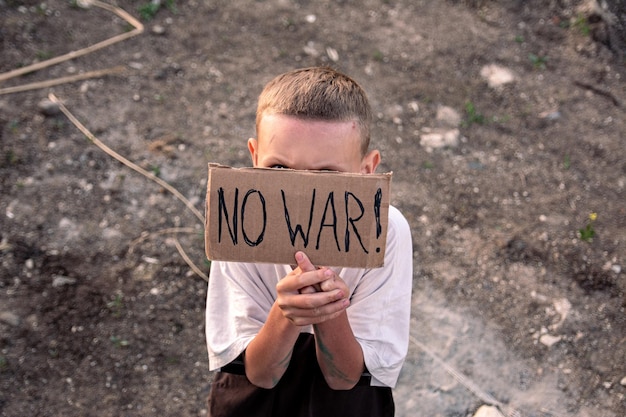 Um menino com um rosto sujo e olhos tristes segura um cartaz de papelão com a inscrição no war