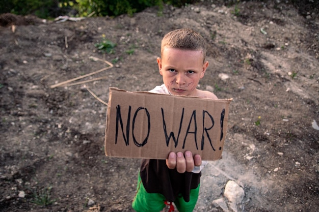 Um menino com um rosto sujo e olhos tristes segura um pôster de papelão com a inscrição no war em inglês