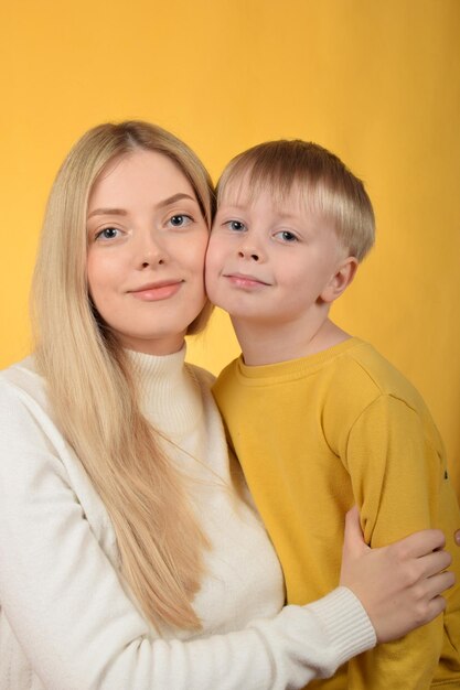 Um menino com uma camisa amarela está de pé com sua mãe em um fundo amarelo