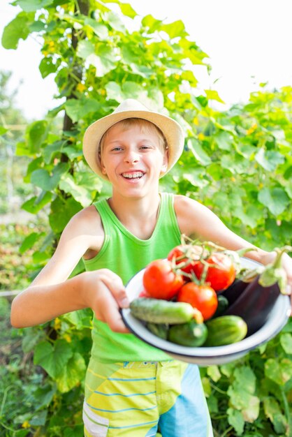 Um menino com uma tigela de legumes no jardim