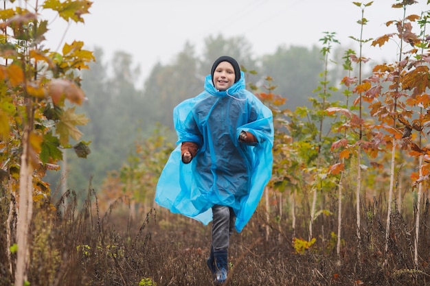 Um menino corre em uma capa de chuva perto das árvores