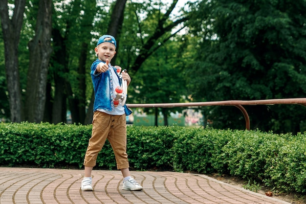 Um menino da cidade pequena e um skate. Um jovem está de pé no parque e segurando um skateboar