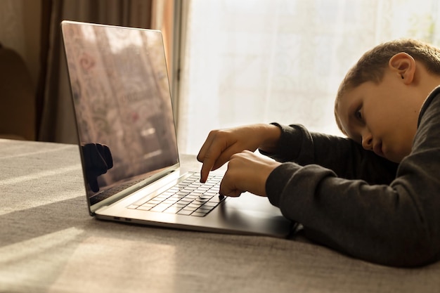 Um menino de 10 anos estuda online e adormece de cansaço ou preguiça na frente de um laptop