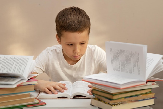 Um menino de 10 anos lê e estuda cuidadosamente em uma mesa com pilhas de livros