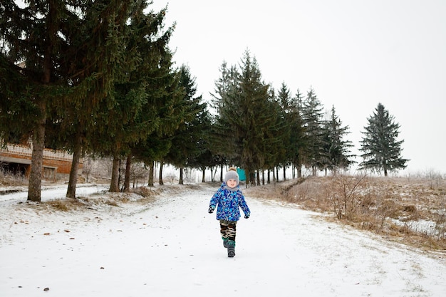 Um menino de 3 anos corre na neve no inverno e se alegra em sua infância Roupas quentes de inverno