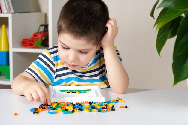 Um menino de 4 anos brinca com um mosaico coleta uma foto de pequenas peças de plástico Desenvolvimento de habilidades motoras finas em crianças