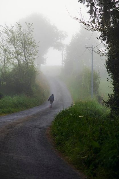 Um menino de 8 anos com uma mochila vai para a escola ao longo de uma estrada rural de manhã sozinho na primavera