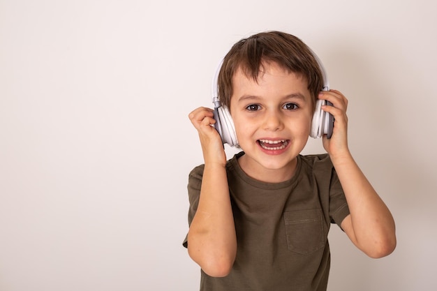 um menino de cabelos escuros em uma camiseta cáqui ouve música com fones de ouvido e ri