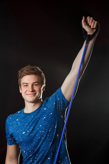 Um menino de camiseta azul em pé e sorrindo com equipamento de fitness na mão