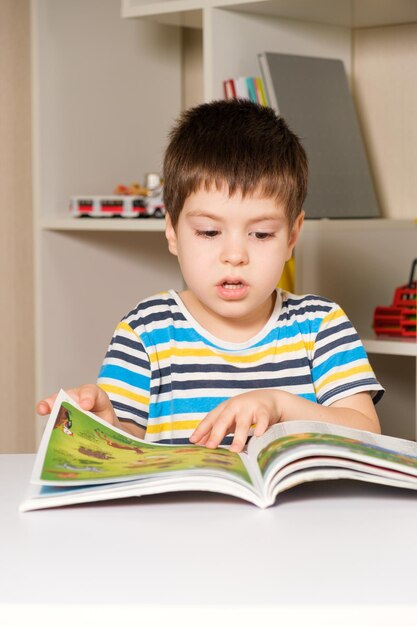 Um menino de camiseta listrada lê um livro, folheia páginas com fotos