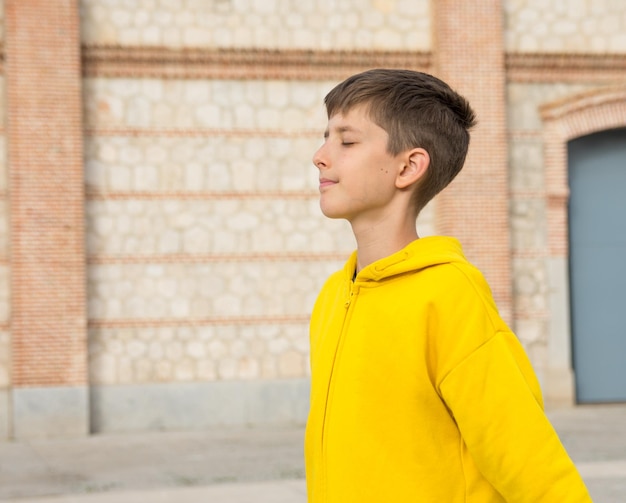 um menino de capuz amarelo está andando na frente de uma parede de tijolos