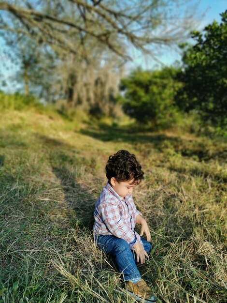 Foto um menino de comprimento completo sentado na grama no parque