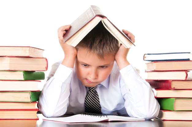 Um menino de escola cansado e atrasado senta-se em uma biblioteca com livros e aprende lições. Relutância em aprender.