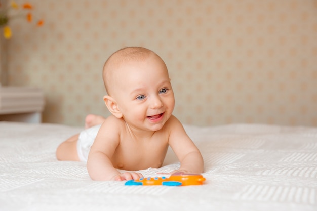 Um menino de fralda e chocalho na cama está deitado de bruços