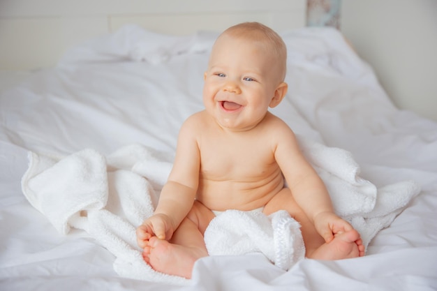 Um menino de fralda está sentado na cama coberto com uma toalha depois de tomar banho no quarto