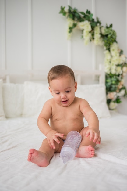 Um menino de fralda está sentado na cama com uma garrafa de água