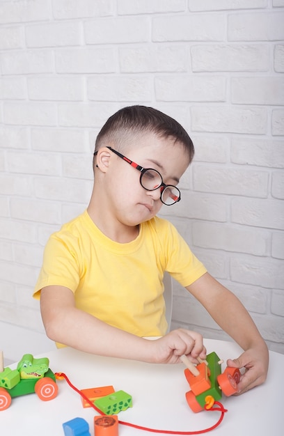 Um menino de óculos com síndrome de down senta-se a uma mesa e brinca com brinquedos