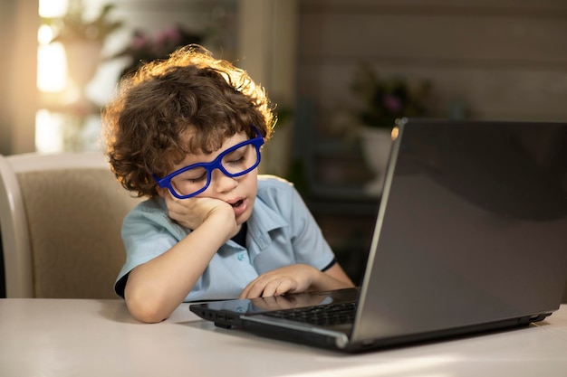 um menino de óculos em casa nos raios do pôr do sol adormeceu perto do laptop