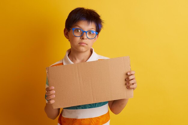 Um menino de óculos em um fundo amarelo com emoções diferentes segura um banner de papelão