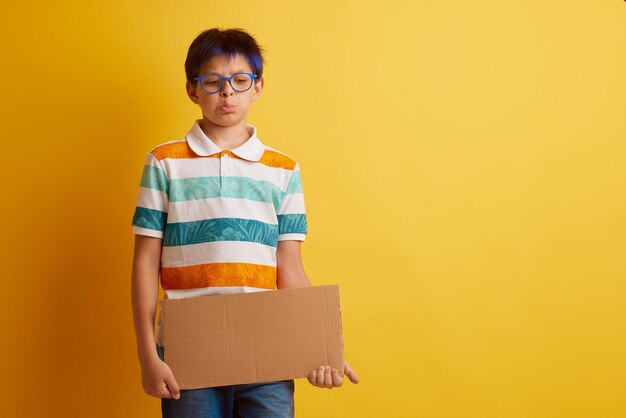 um menino de óculos em um fundo amarelo segura um banner de papelão com um espaço vazio para texto