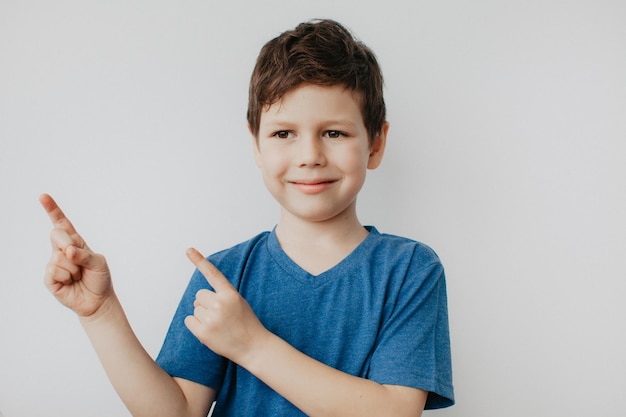 Foto um menino de pré-escola com uma camiseta azul em um fundo claro mostra uma foto de alta qualidade com os polegares para cima