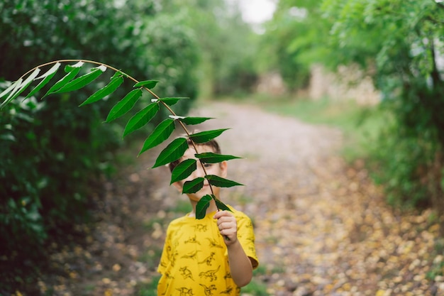 Um menino de seis anos corre com folhas verdes nas mãos no campo Menino feliz rindo e brincando no dia de verão