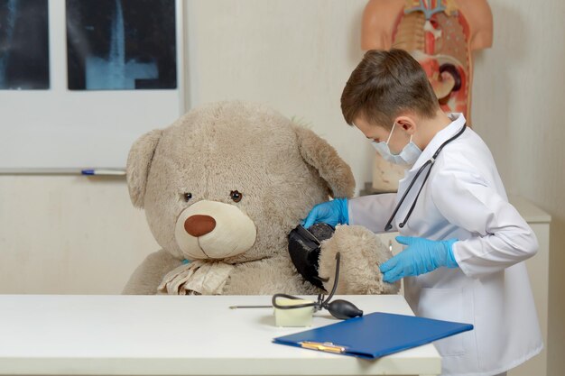 Um menino de terno médico mede a pressão de um ursinho de pelúcia