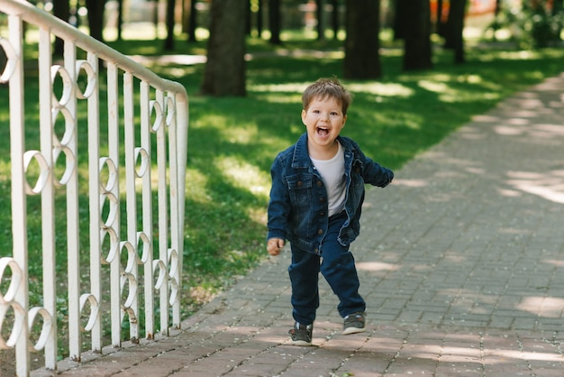 Um menino de três anos corre por um parque de verão e ri