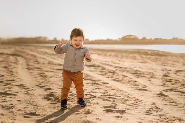 Um menino de um ano aprende a andar na areia à beira do rio.