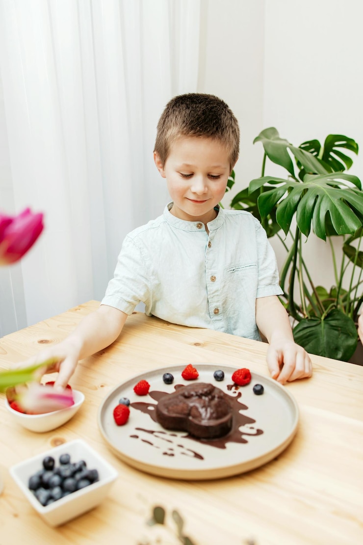 Foto um menino decora um bolo de chocolate em forma de coração para o dia das mães com bagas frescas para o dia dos namorados