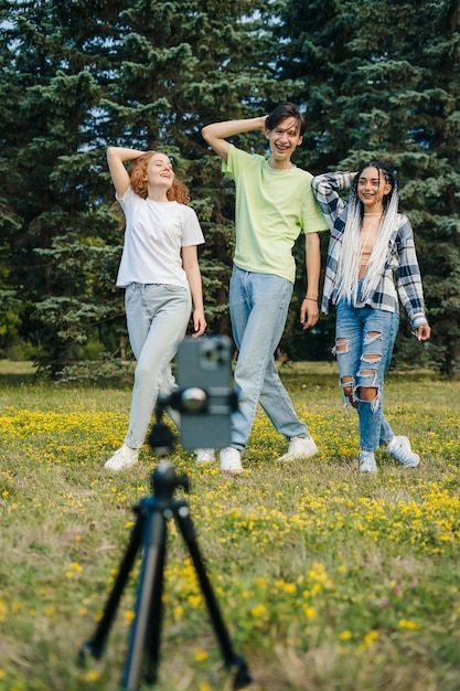 Um menino e duas meninas da geração digital alfa torcendo e dançando na frente de um telefone com câmera enquanto passam o fim de semana no parque da cidade Estilo de vida jovem Amigos felizes juntos
