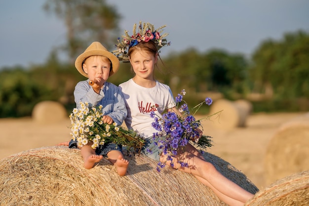 Um menino e uma menina estão sentados em um palheiro com um buquê de flores Crianças na natureza Estilo de vida